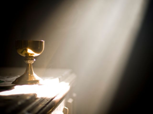 A gold chalice in an altar with ray of light shining on it.