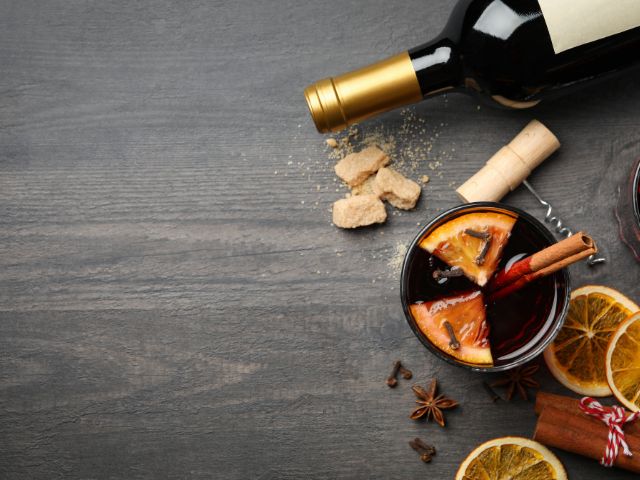 A cup of mulled wine and various ingredients for making it in a wooden background.