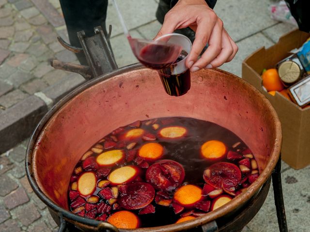 Warm mulled wine in a pot being served in a glass cup.