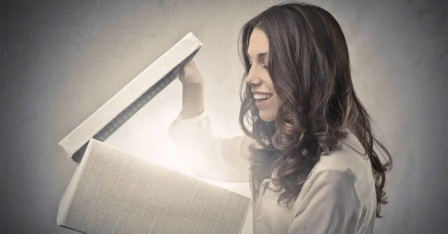 Woman opening a box with light coming out of it, with an excited look on her face.